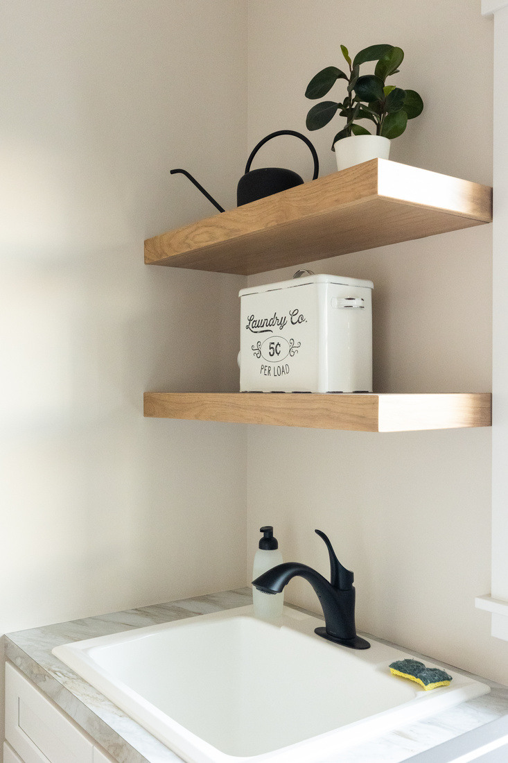 Compact laundry area with floating shelves and utility sink in West Michigan by Ridgewood Home Construction