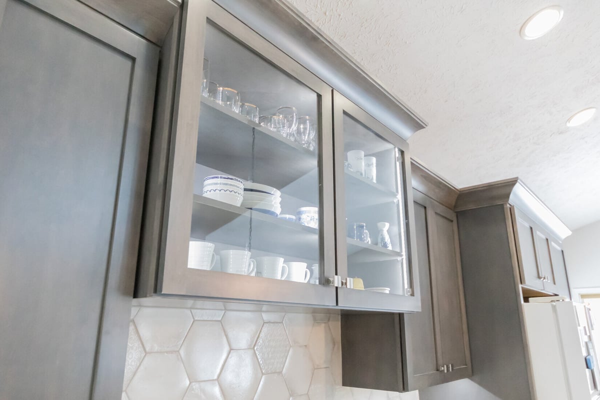 Glass-front upper cabinets with dishes and mugs in Ridgewood Home Construction’s Cascade kitchen remodel