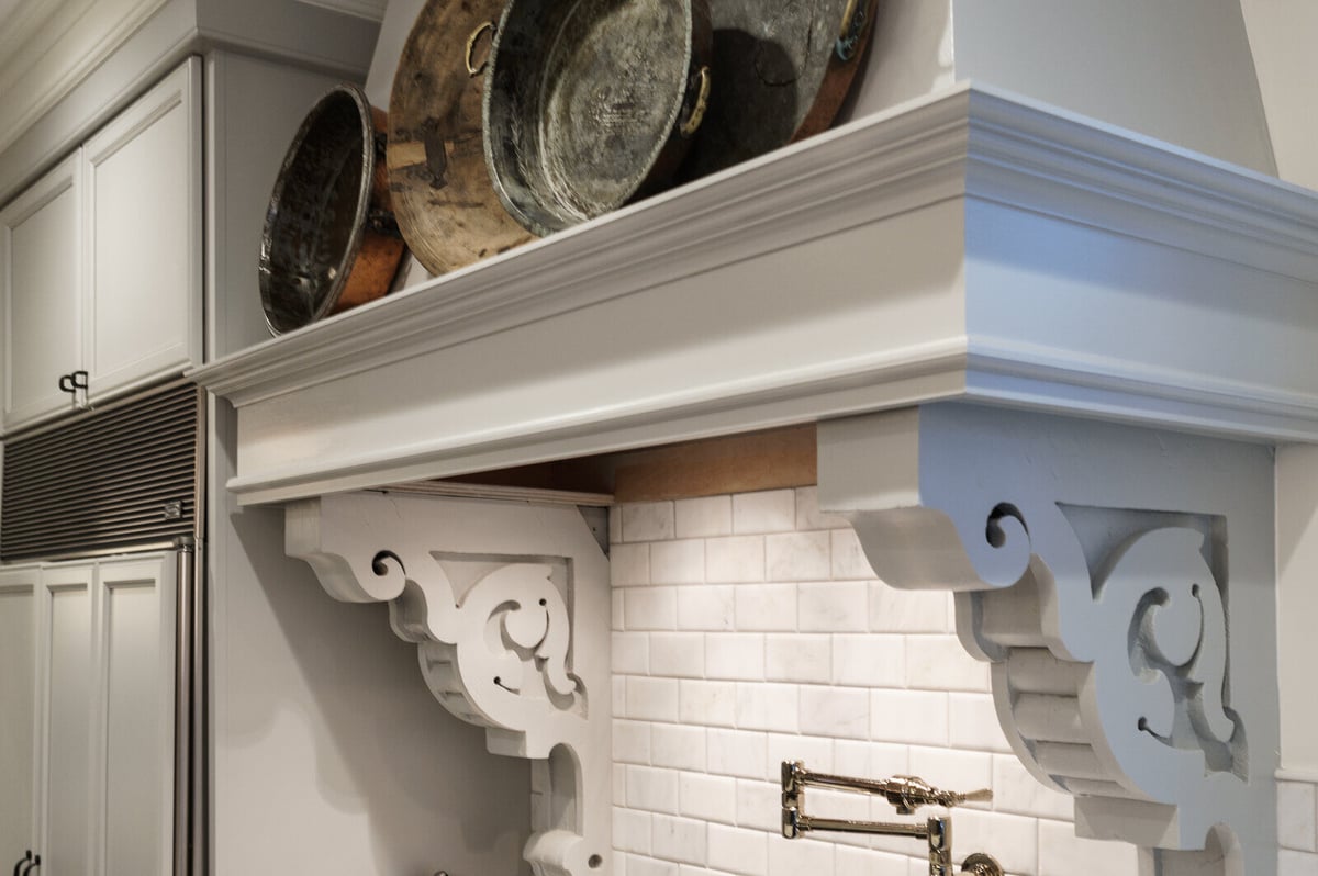 Close-up of custom range hood with antique pans and ornate brackets in East Grand Rapids kitchen remodel by Ridgewood Home Construction
