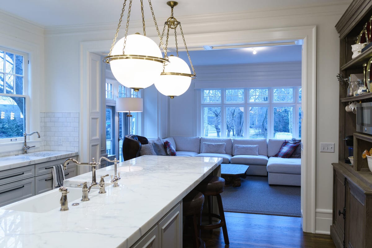 Transitional kitchen and living room view with marble island and pendant lights by Ridgewood Home Construction in East Grand Rapids