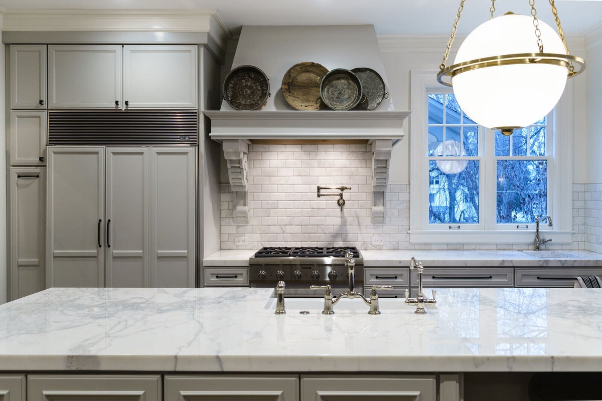 Wide view of kitchen remodel in East Grand Rapids with marble island and brass lighting by Ridgewood Home Construction