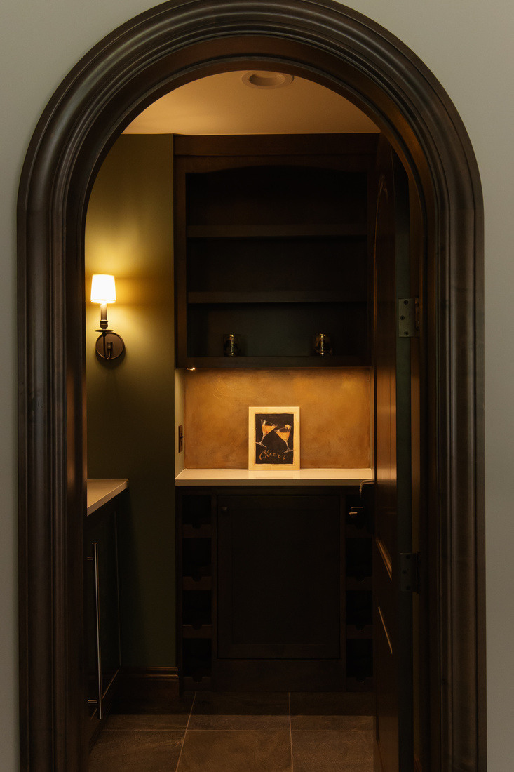 Dark arched entryway leading to stylish basement bar nook with “Cheers” decor by Ridgewood Home Construction in Grand Rapids Township