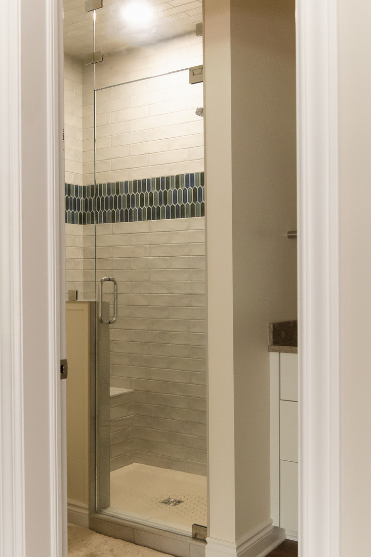 Modern glass shower with accent tile band in basement bathroom remodel by Ridgewood Home Construction in Grand Rapids Township